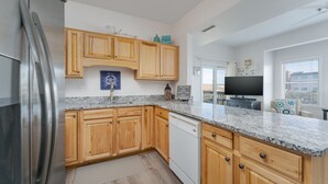 Una cocina moderna con armarios de madera, encimeras de granito, un refrigerador de acero inoxidable y un lavavajillas.