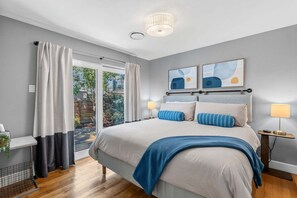 A modern bedroom with a large bed, two bedside lamps, and a view of the outdoors through a sliding door. - Littleton Cottage🏡2 blocks to Main🛍️Pets🐶Fenced Yard♨️Firepit🤑0 Cleaning & Pet Fee (Littleton)