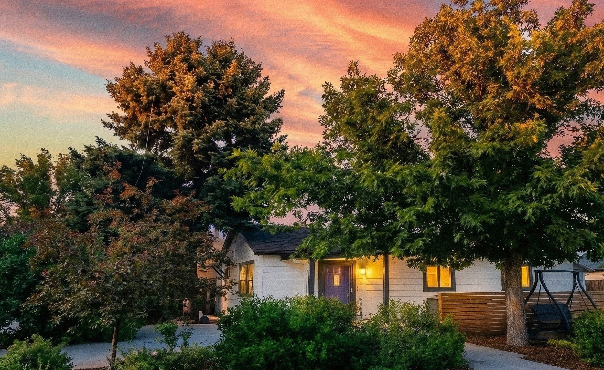 A single-story house with a dark roof, surrounded by mature trees and a well-maintained lawn.