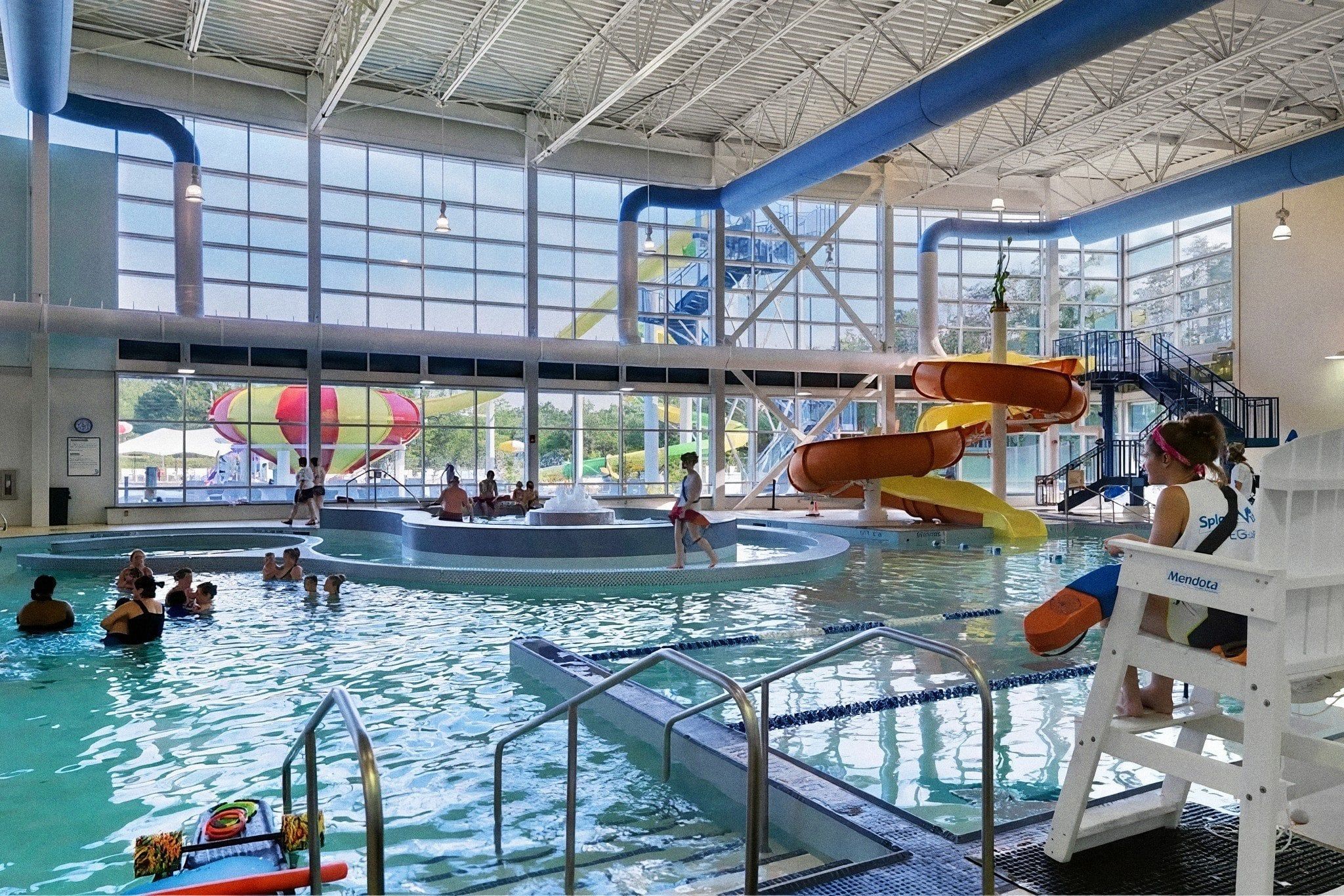 An indoor swimming pool with multiple lanes, a water slide, and a lifeguard stand.