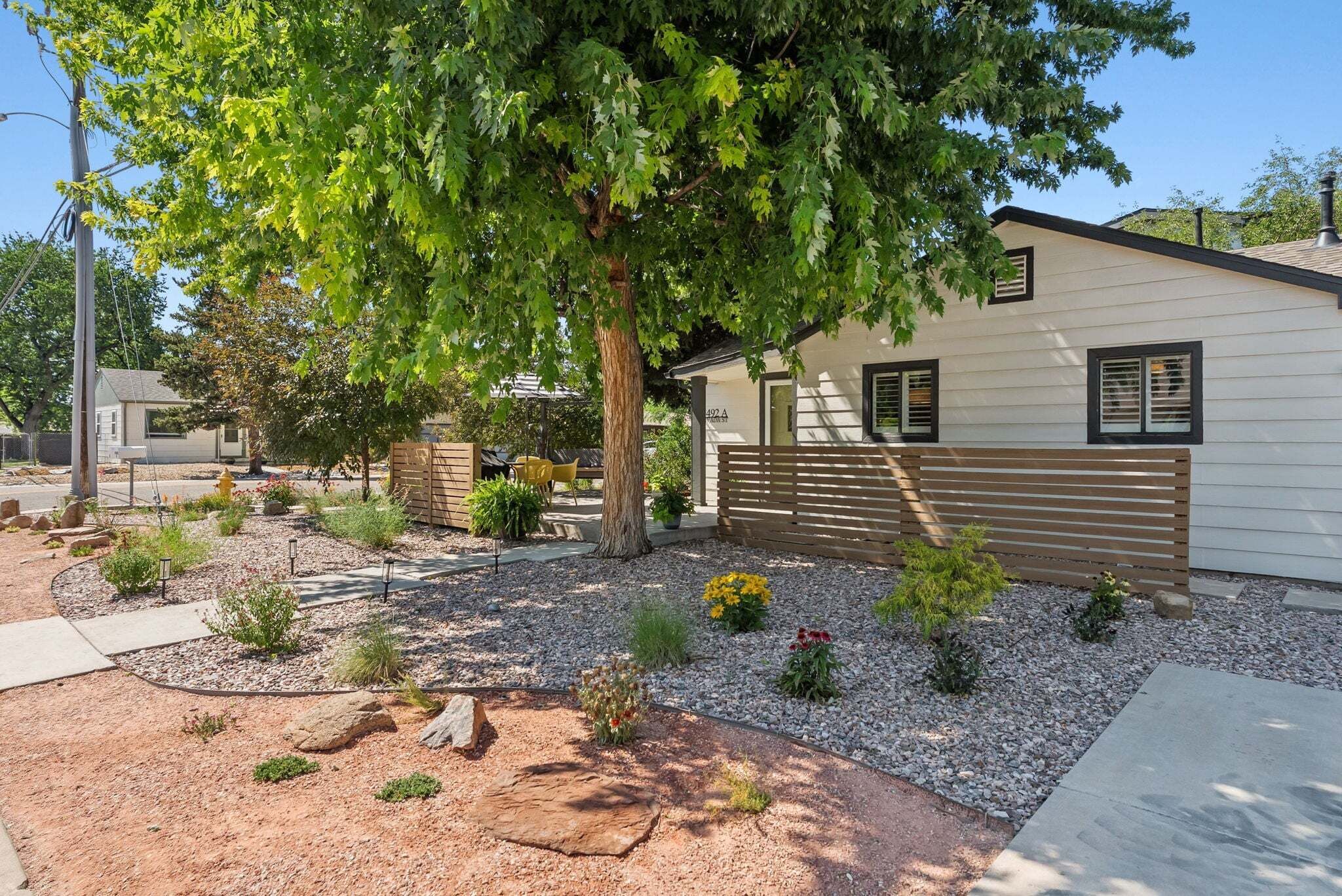 A residential property with a paved driveway, a wooden bench, a small garden with gravel and plants, and a house with a light-colored exterior and a dark roof.