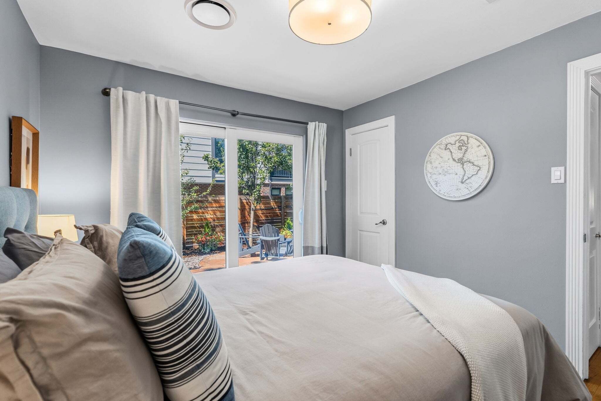 A bedroom with a bed, a view of the outdoors, a door, and a wall-mounted globe.