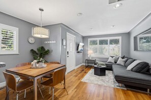 A modern living room with a dining area, grey walls, wooden flooring, and a grey sofa. - Littleton Cottage🏡2 blocks to Main🛍️Pets🐶Fenced Yard ♨️Firepit🤑0 Cleaning & Pet Fee (Littleton)