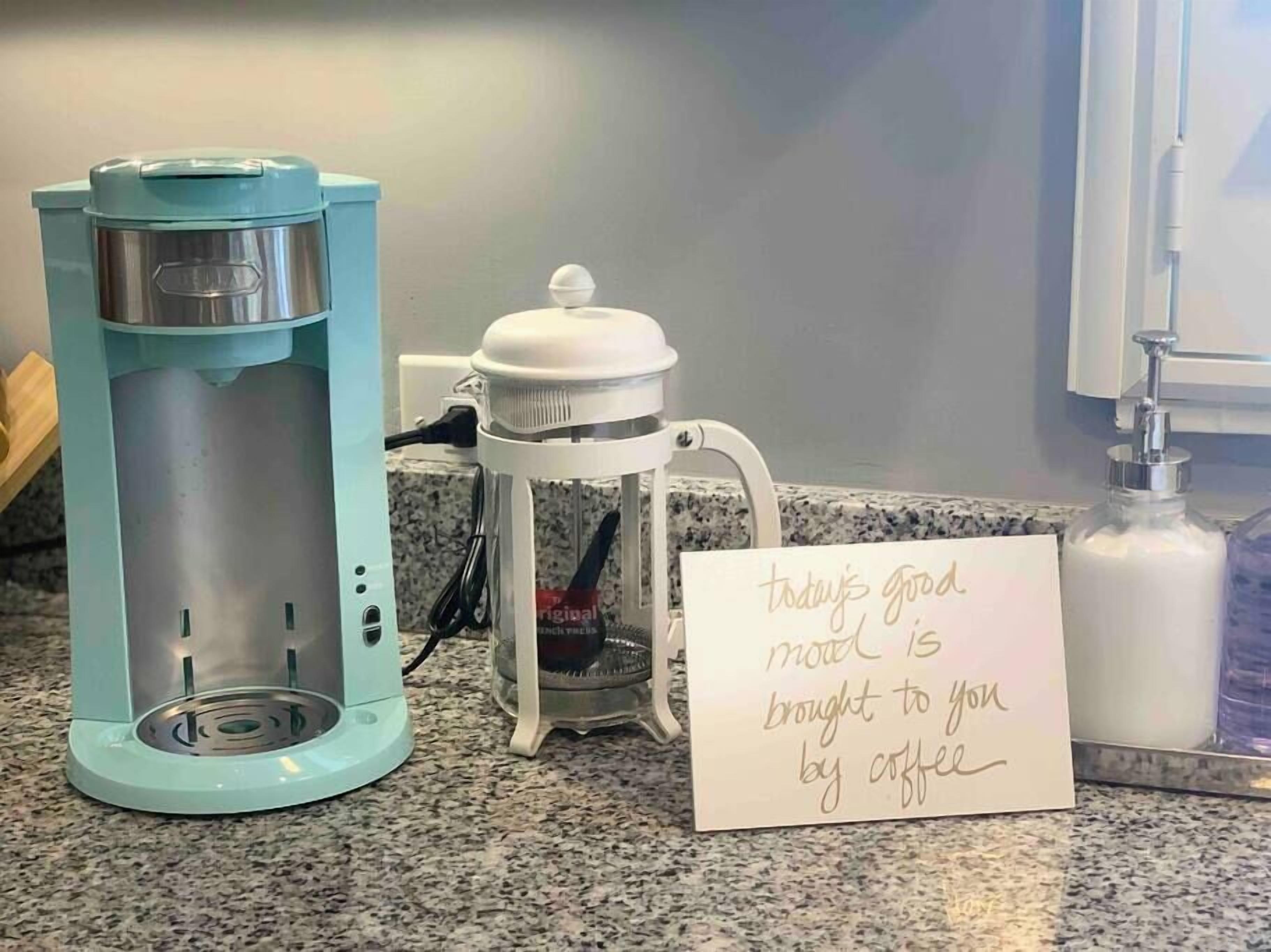 A coffee maker, a French press, and a note on a countertop.