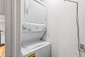 A white washing machine with control knobs and a yellow caution sign. - Littleton Cottage🏡2 blocks to Main🛍️Pets🐶Fenced Yard♨️Firepit🤑0 Cleaning & Pet Fee (Littleton)