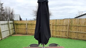 A wooden patio table with four chairs and a black umbrella, surrounded by a brick patio.