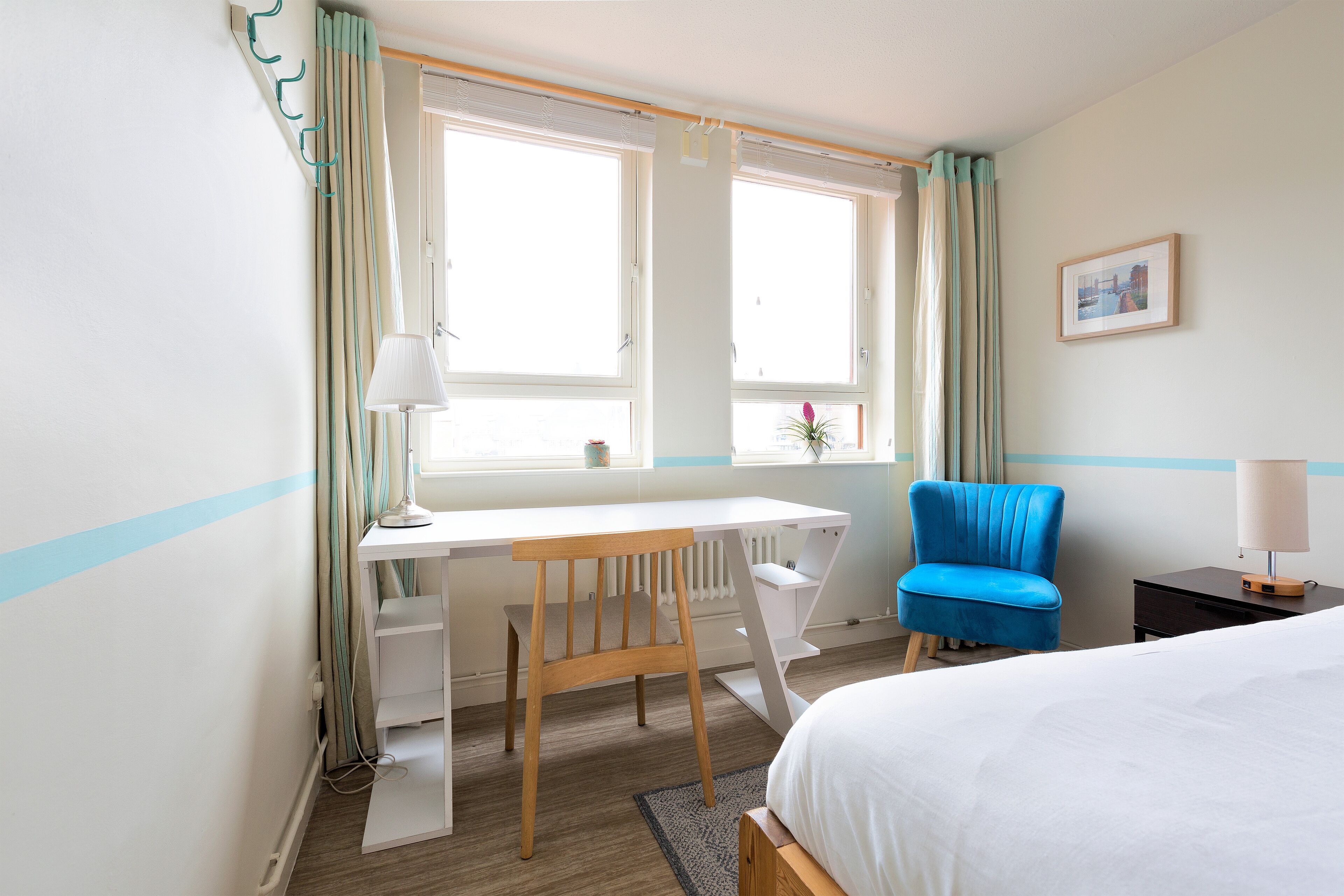 A bedroom with a bed, a desk, a chair, and a window with curtains.