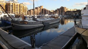 A marina with boats docked, a wooden dock, and buildings in the background. - St Katharine Dock | By Tower Bridge | Dock View (London)