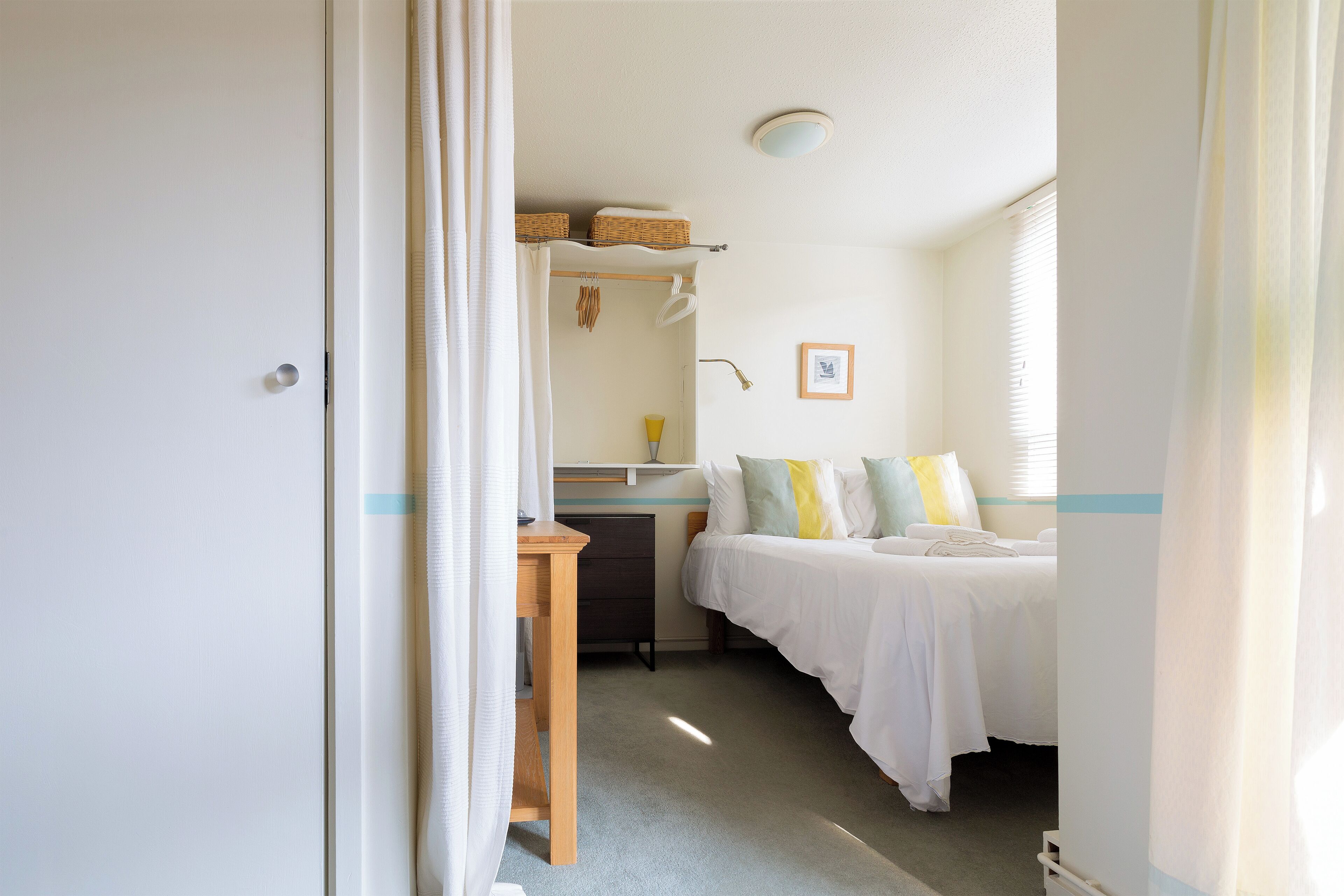 A small, well-lit bedroom with a single bed, a desk, and a window.