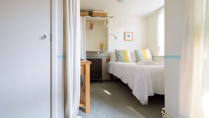 Een kleine, goed verlichte slaapkamer met een enkel bed, een bureau en een raam.