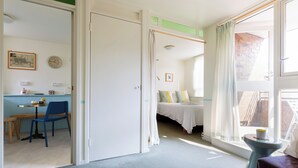 Een kamer met een bed, een raam met gordijnen, een klein tafeltje en een stoel.