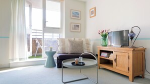 Een woonkamer met een bank, een salontafel, een tv op een houten kast en een raam met uitzicht.