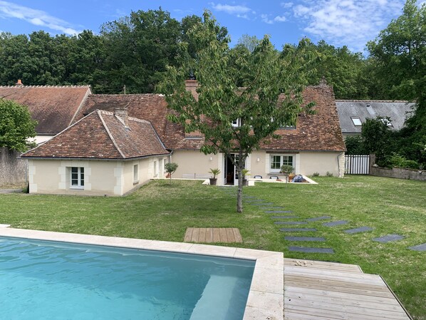 A residential property with a swimming pool, a small garden, and a brick house with a tiled roof.