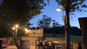 An outdoor patio with a wooden table and chairs, a barrel, and a wooden fence.