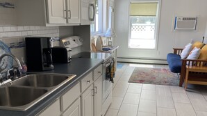 A kitchen with white cabinets, a stainless steel sink, a coffee maker, and a toaster. There is a window with a view of a fence outside. - Seashell Cottages/JK Rentals -  The Daniel Unit (Old Orchard Beach)