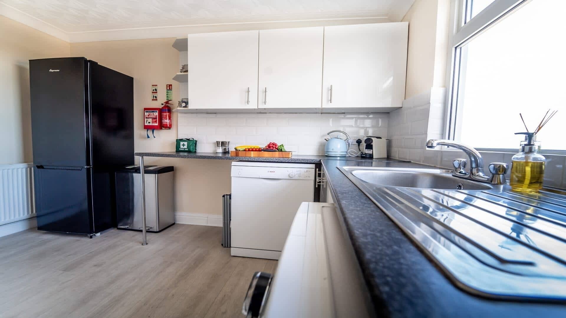A modern kitchen with a black refrigerator, white cabinets, a dishwasher, and a sink with a window view.