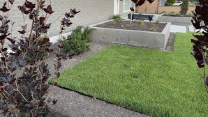 Una propiedad residencial con un césped cuidado, fachada de ladrillo y un pequeño jardín con diversas plantas.