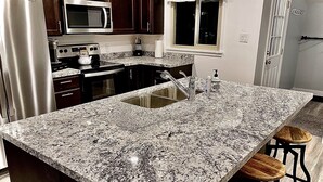 Una cocina con encimeras de granito, electrodomésticos de acero inoxidable y una isla grande con taburetes de bar.