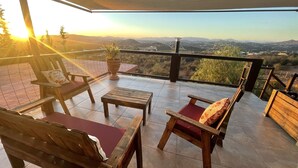 A terrace with wooden furniture, a potted plant, and a view of distant mountains.