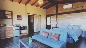 A spacious room with a large bed, a sofa, a wooden ceiling, and a kitchen area.