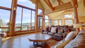 Ein geräumiges Wohnzimmer mit großen Fenstern, Holzbalken und einer gemütlichen Sitzecke mit Couchtisch.