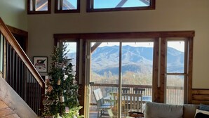 Ein geräumiges Wohnzimmer mit einer Holztreppe, einem Weihnachtsbaum, einer großen Schiebeglastür, die auf eine Terrasse führt, und einem Deckenventilator.