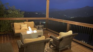 Eine Terrasse mit Korbmöbeln, einer Feuerstelle und Blick auf die Berge in der Nacht.