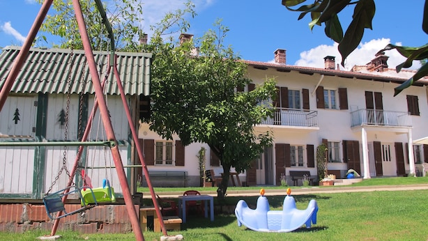 Una casa de dos pisos con un balcón, un columpio y un árbol pequeño en el jardín.