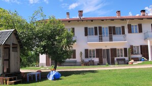 Un edificio de dos pisos con un balcón, un cobertizo pequeño y un árbol en el patio.