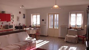 Una sala de estar con un sofá, una mesa de comedor y una silla. Hay una zona de cocina con un microondas y armarios.