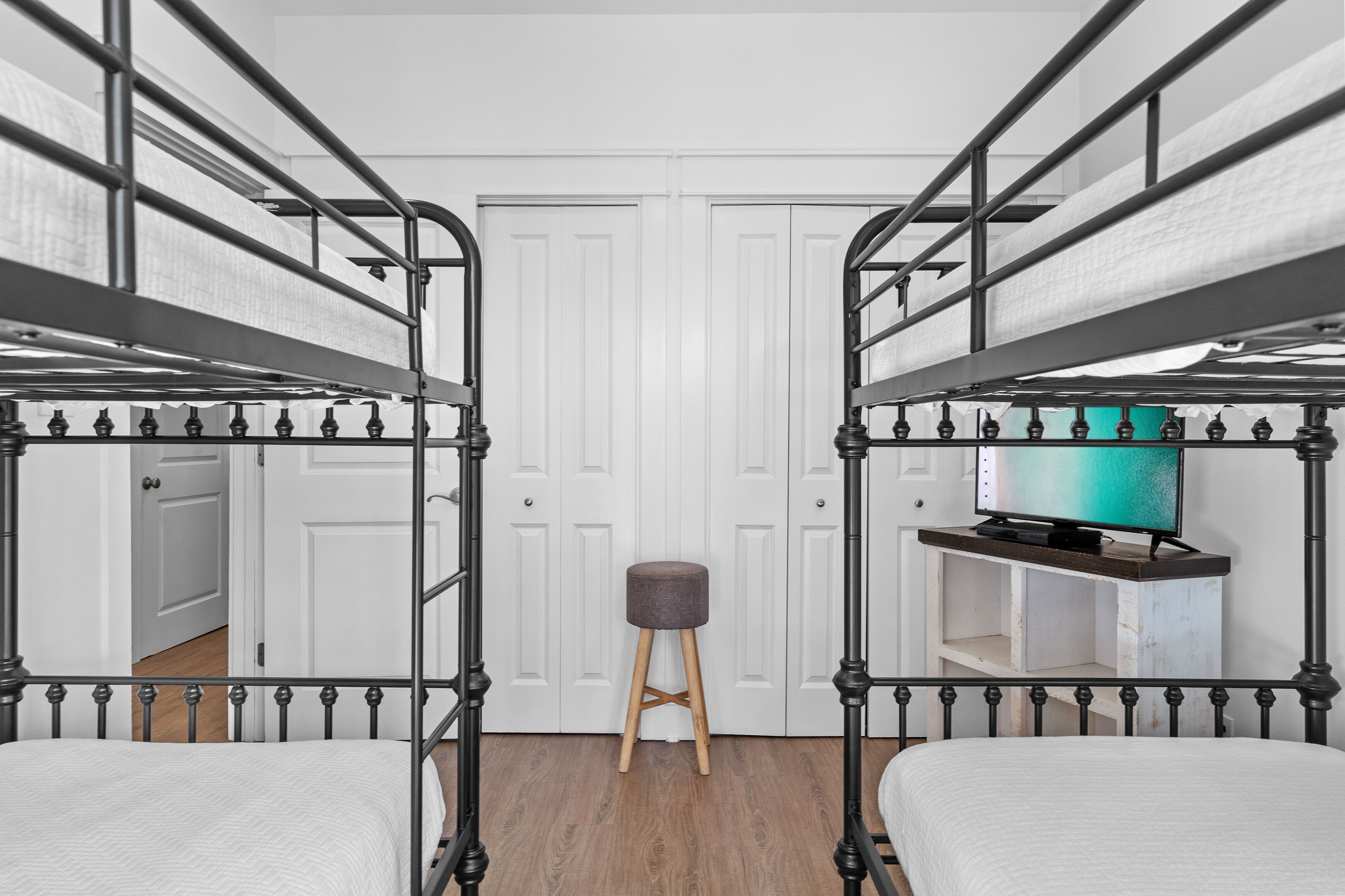 A bunk bed room with a television on a wooden shelf, a stool, and a white door.