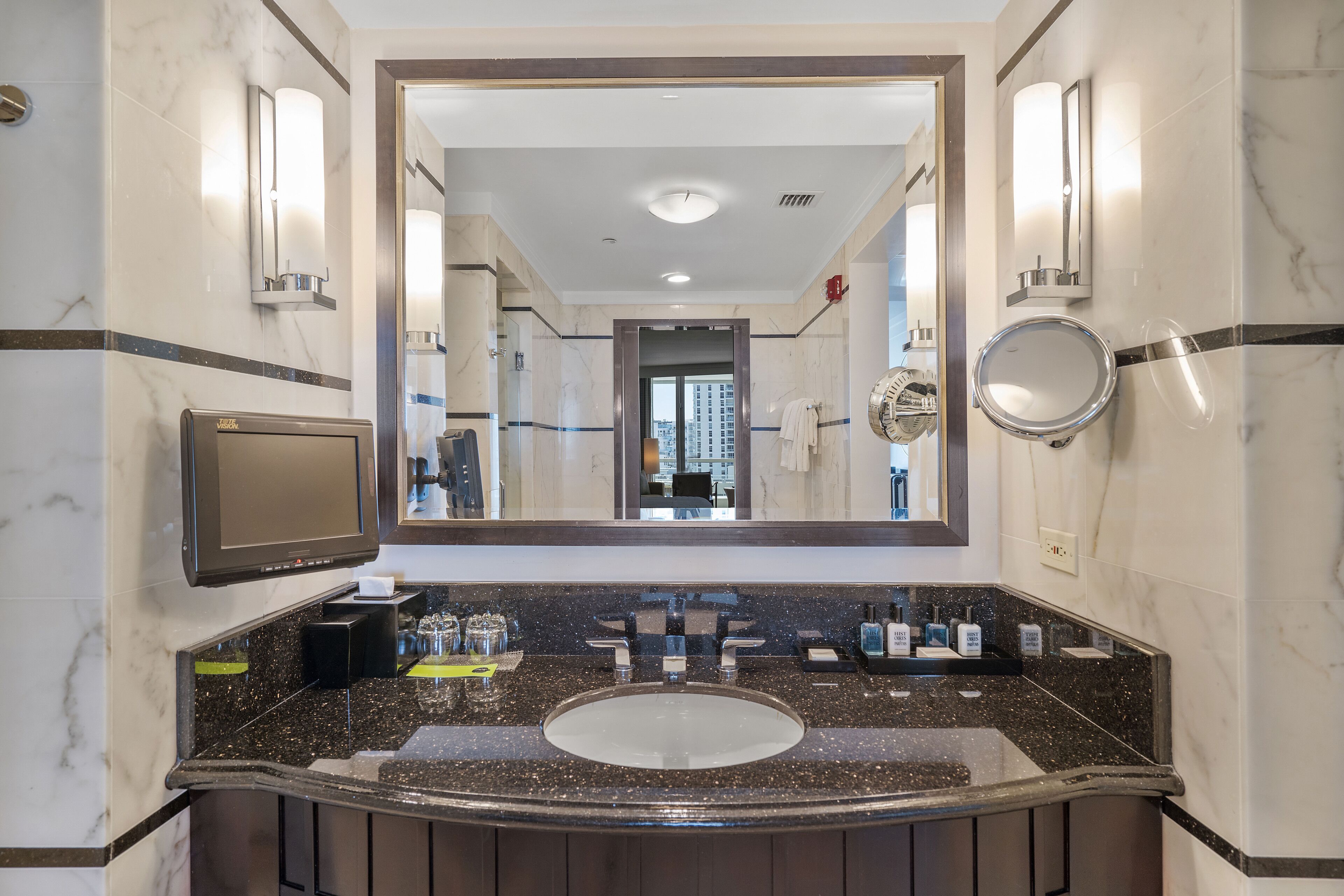 A modern bathroom with a large mirror, a sink with a marble countertop, and wall-mounted lighting.
