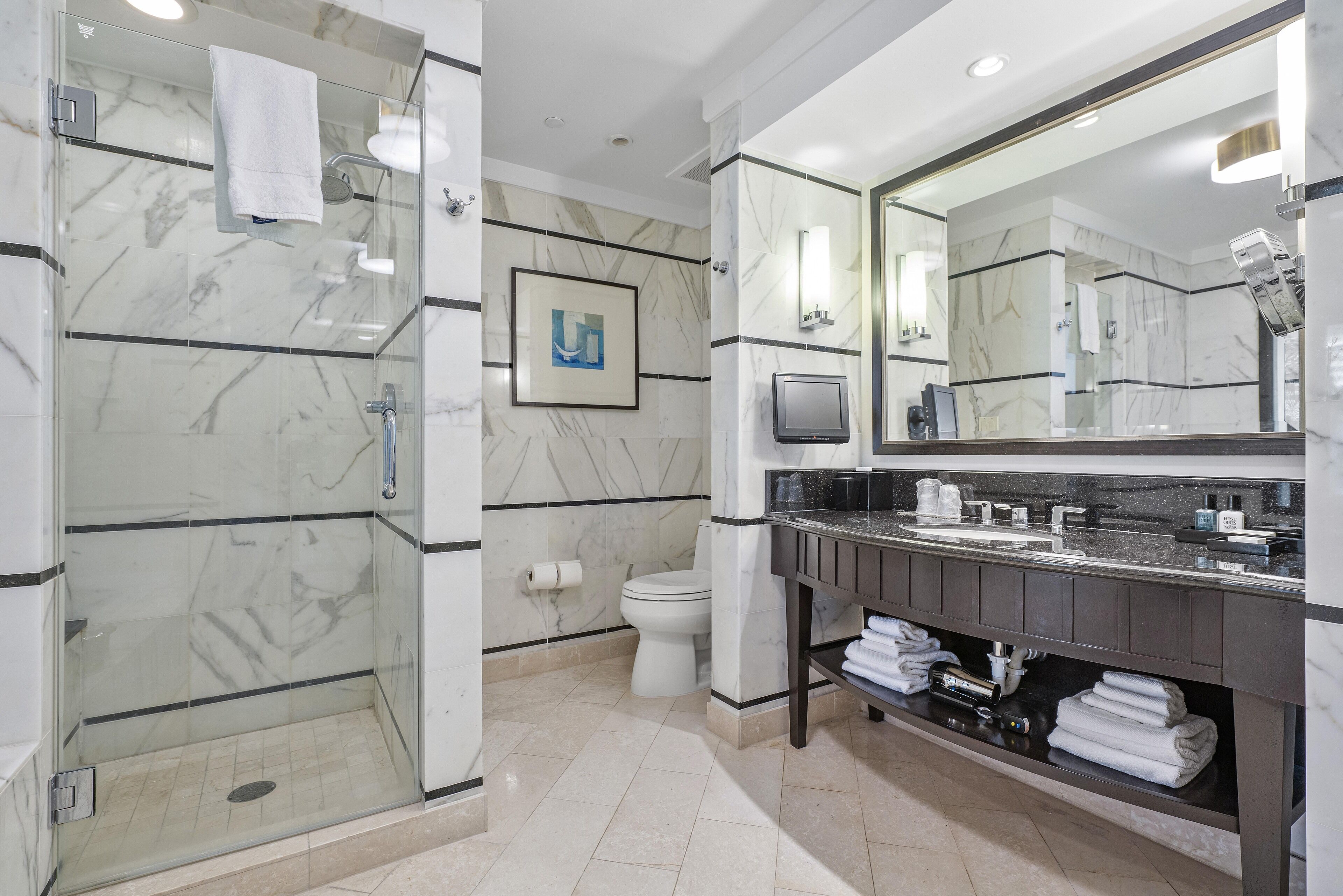 Un baño moderno con cabina de ducha de vidrio, un espejo grande y un revestimiento de mármol.