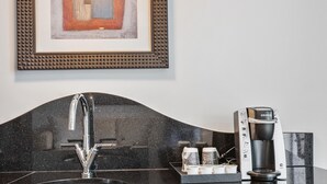 Una cucina moderna con un piano di lavoro nero, lavello in acciaio inossidabile e una macchina per caffè Keurig.