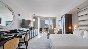 Camera d'albergo con un letto grande, una scrivania con sedie, una TV e vista sulla città da ampie finestre.