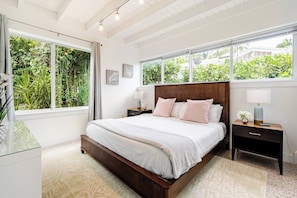Quarto com uma cama grande, duas mesas de cabeceira e vista para o verde pelas janelas.