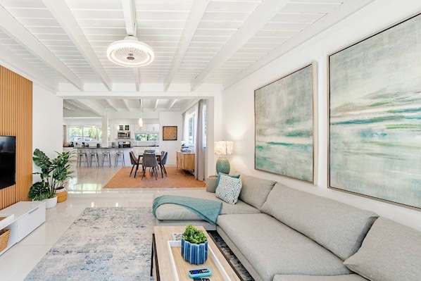 A modern living room with a sofa, a coffee table, and a TV. There is a dining area with a table and chairs in the background. - Bright & Spacious 4 mi to BEACH +Big Backyard (Miami)