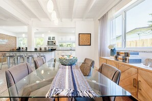 A modern kitchen with white cabinets, a central island, and a dining area with a glass table and chairs. - Bright & Spacious 4 mi to BEACH +Big Backyard (Miami)
