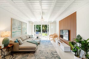 A modern living room with a sectional sofa, a coffee table, a TV, and a large window. - Bright & Spacious 4 mi to BEACH +Big Backyard (Miami)