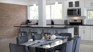 Une cuisine moderne avec des meubles blancs, un îlot central et un coin repas comprenant une table et des chaises en verre.