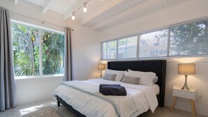 Une chambre avec un grand lit, deux lampes de chevet, une fenêtre avec des stores et une vue sur la verdure.