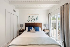 Une chambre à coucher avec un grand lit, deux tables de chevet, une tête de lit et une vue sur l’extérieur, accessible par une porte-fenêtre coulissante.