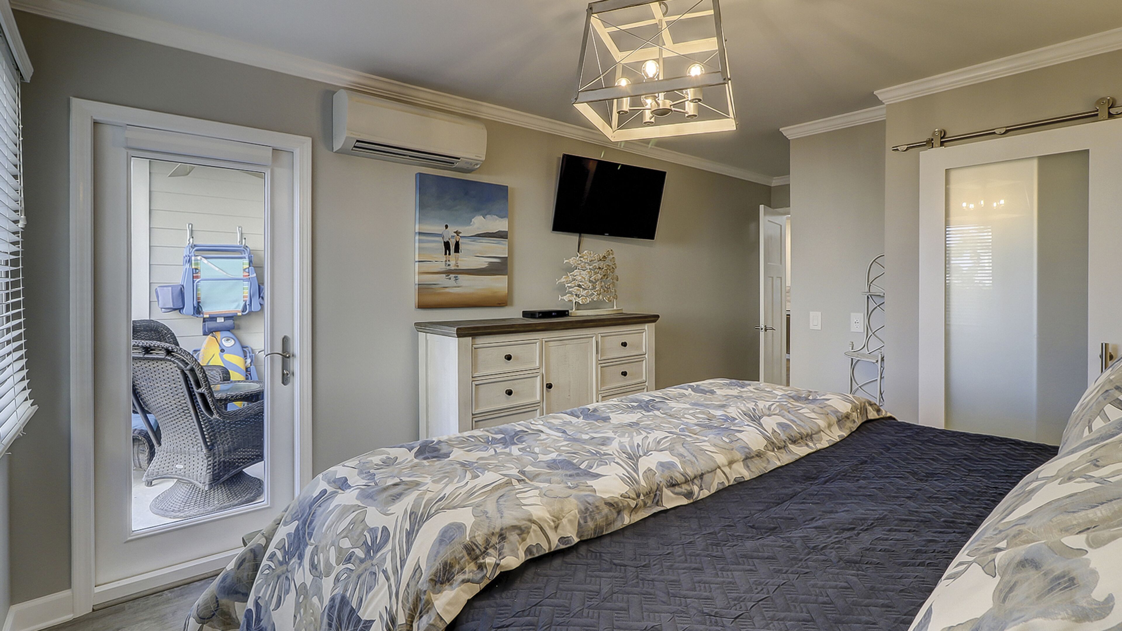 Een slaapkamer met een bed, een dressoir, een televisie en een deur naar een balkon.