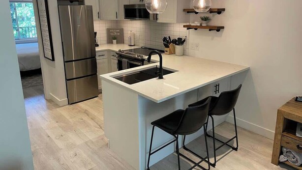 Une cuisine moderne dotée d’un îlot central, d’appareils électroménagers en acier inoxydable et de tabourets de bar.