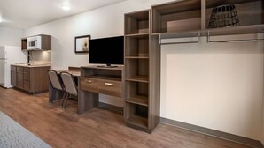 A modern kitchen with built-in appliances, a dining area with a table and chairs, and a large shelving unit with open shelves. - WoodSpring Suites Sulphur - Lake Charles (Sulphur)