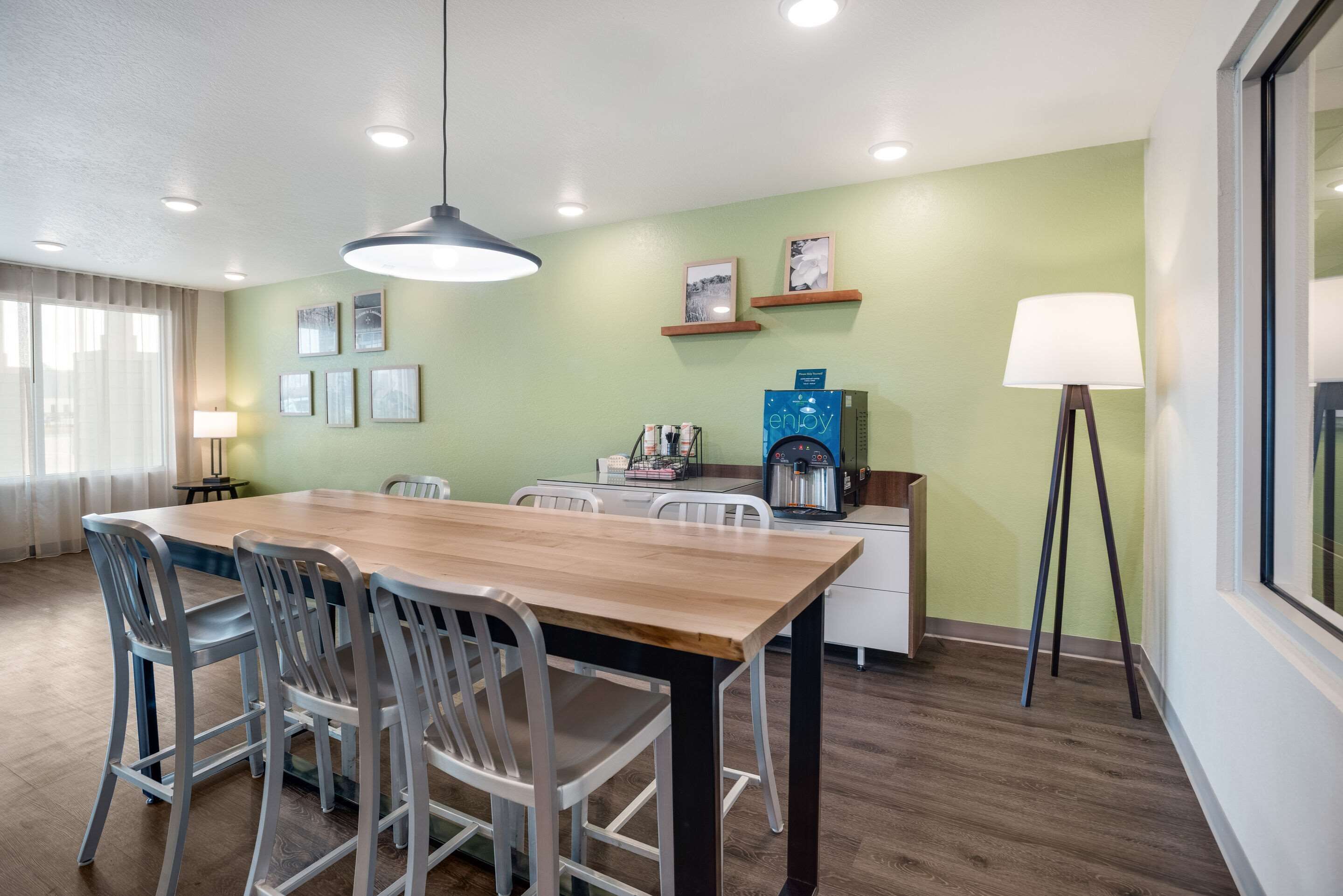 A modern dining area with a wooden table and chairs, a coffee machine, and framed pictures on the wall.