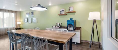 Un espace repas moderne avec une table et des chaises en bois, une machine à café et des tableaux encadrés au mur.