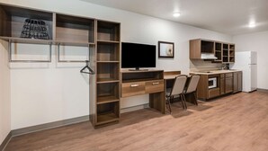 A modern kitchen with wooden cabinetry, a built-in microwave, and a large flat-screen TV. - WoodSpring Suites Sulphur - Lake Charles (Sulphur)