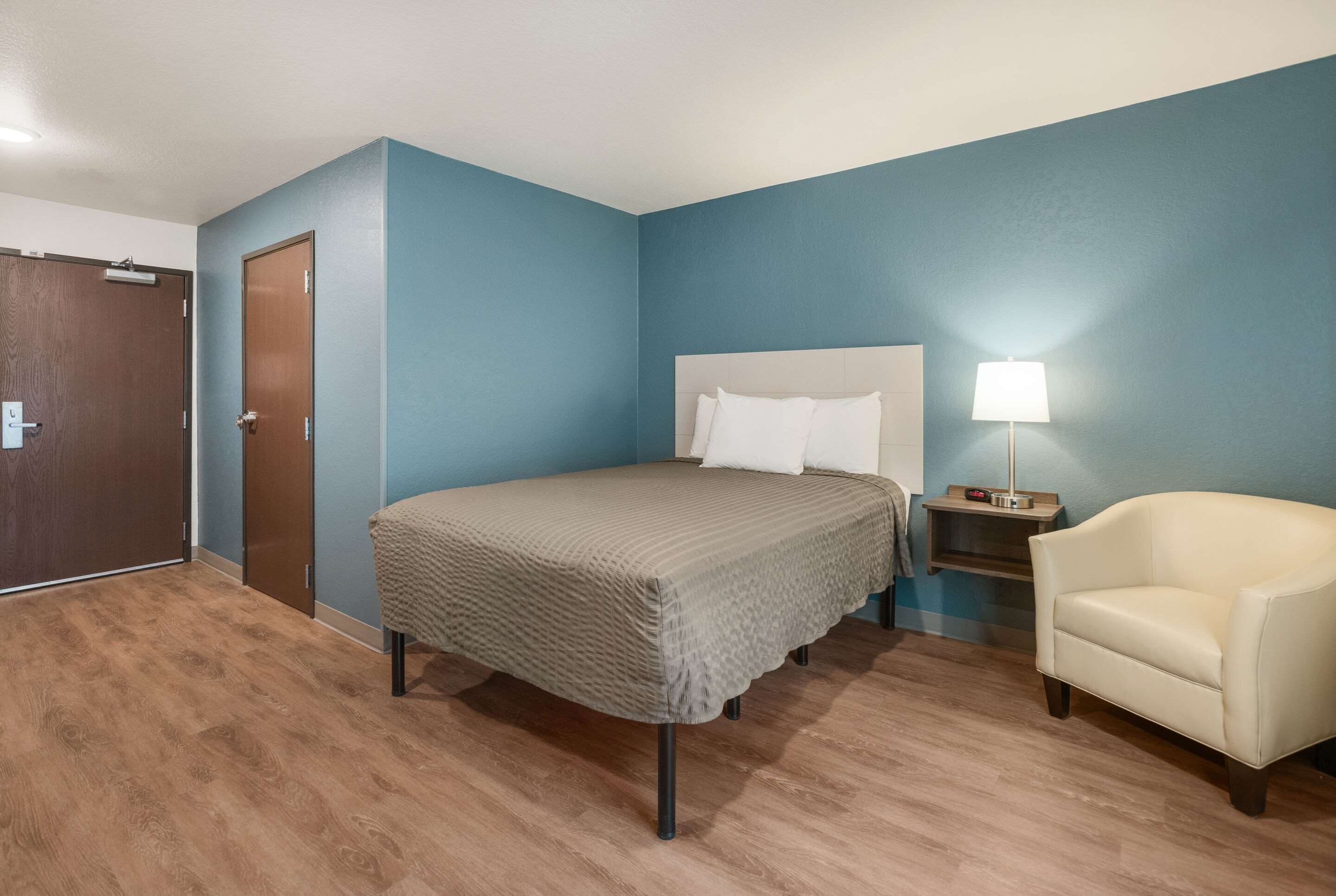 A bedroom with a bed, a chair, a nightstand, and a door.