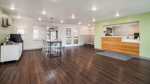 A spacious room with a wooden floor, a reception desk, a dining area with chairs, and a large window. - WoodSpring Suites Sulphur - Lake Charles (Sulphur)